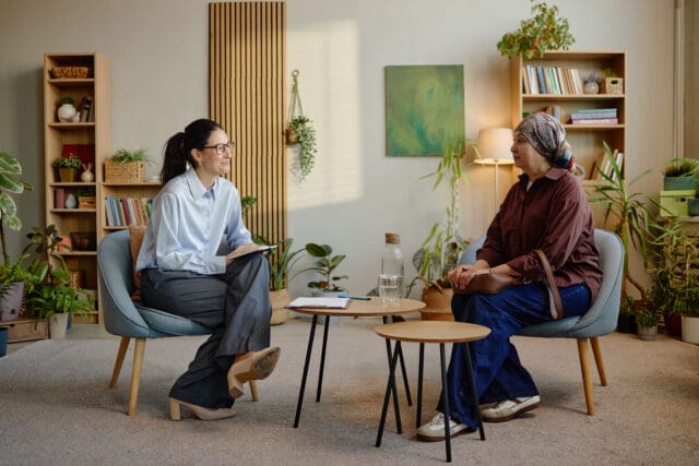 Image displays a therapist and client engaging in a therapy session demonstrating a calm professional approach. Clinical Hypnotherapy is explained in this context as calm, focused and enabling relief from pain and anxiety